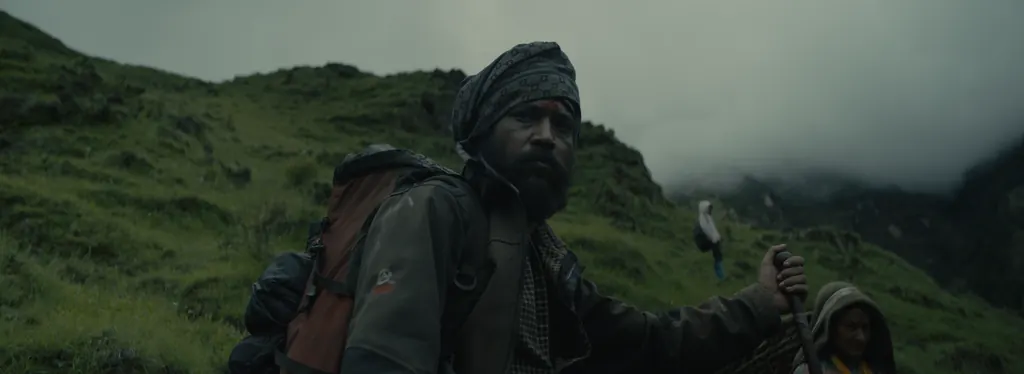 A bearded porter in a turban climbing a green hillside