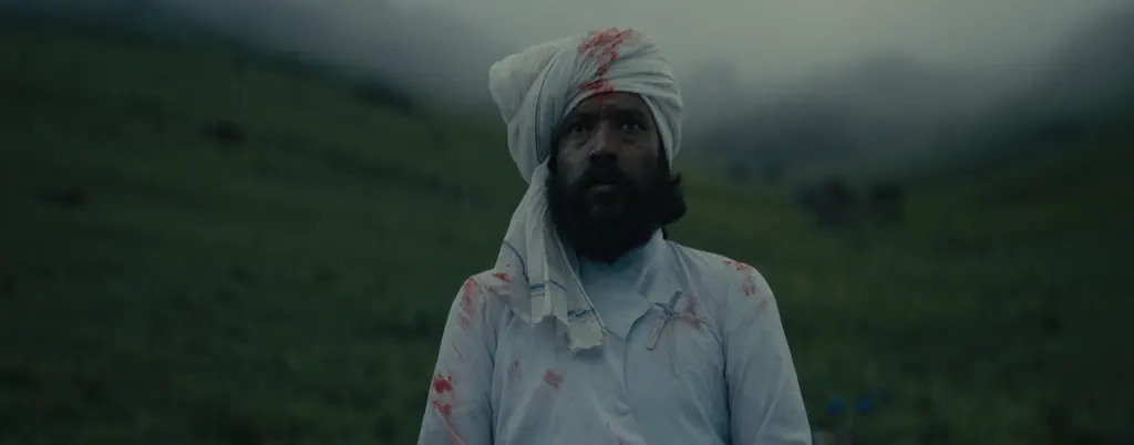 A man in a bloodstained white turban standing in a field