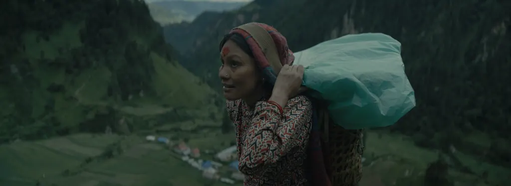 A woman carrying a large bundle above a village in the valley