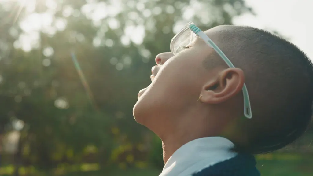 A schoolboy in glasses tilting his face up to the sun