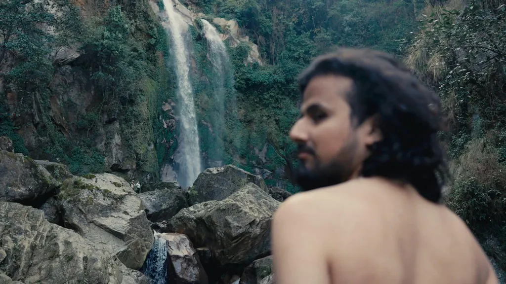 A long-haired man in front of a waterfall