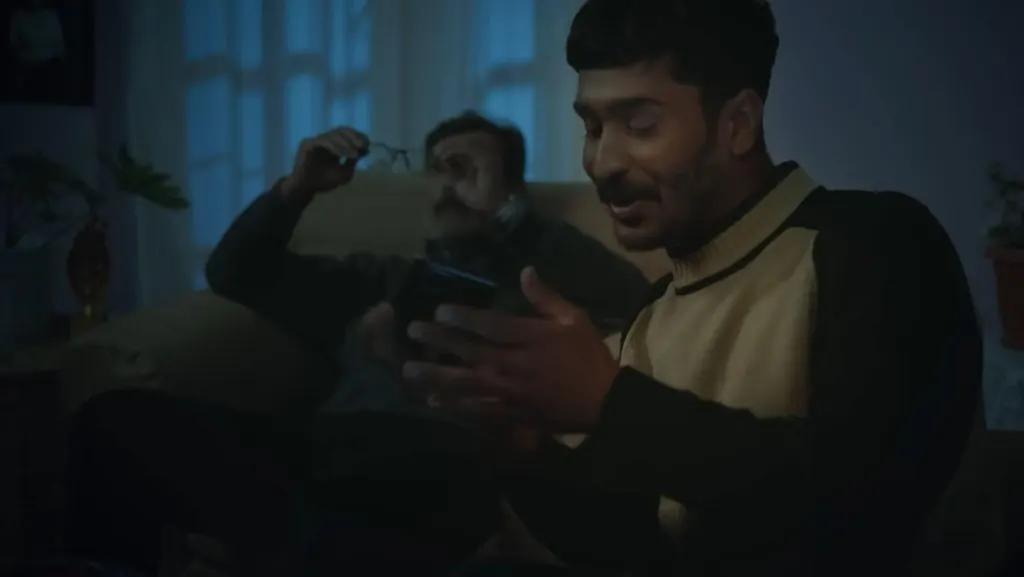 A father and son talking on a sofa, one holding a phone